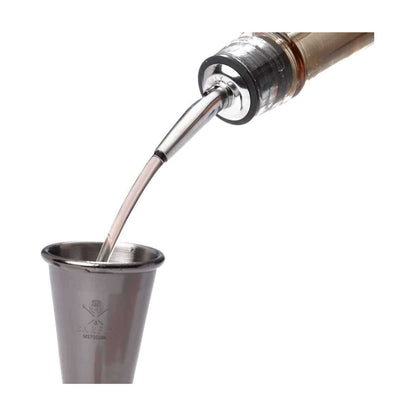A Stainless Barfly Cocktail Liquor Pourer dispensing a stream of brown liquor from a bottle into a stainless steel measuring jigger on a white background