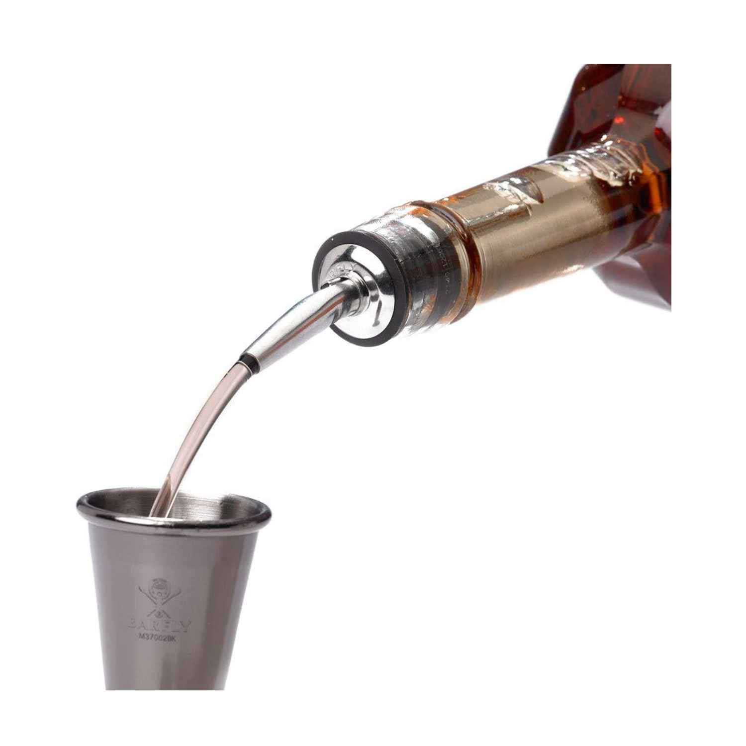 A Stainless Barfly Cocktail Liquor Pourer dispensing a stream of brown liquor from a bottle into a stainless steel measuring jigger on a white background