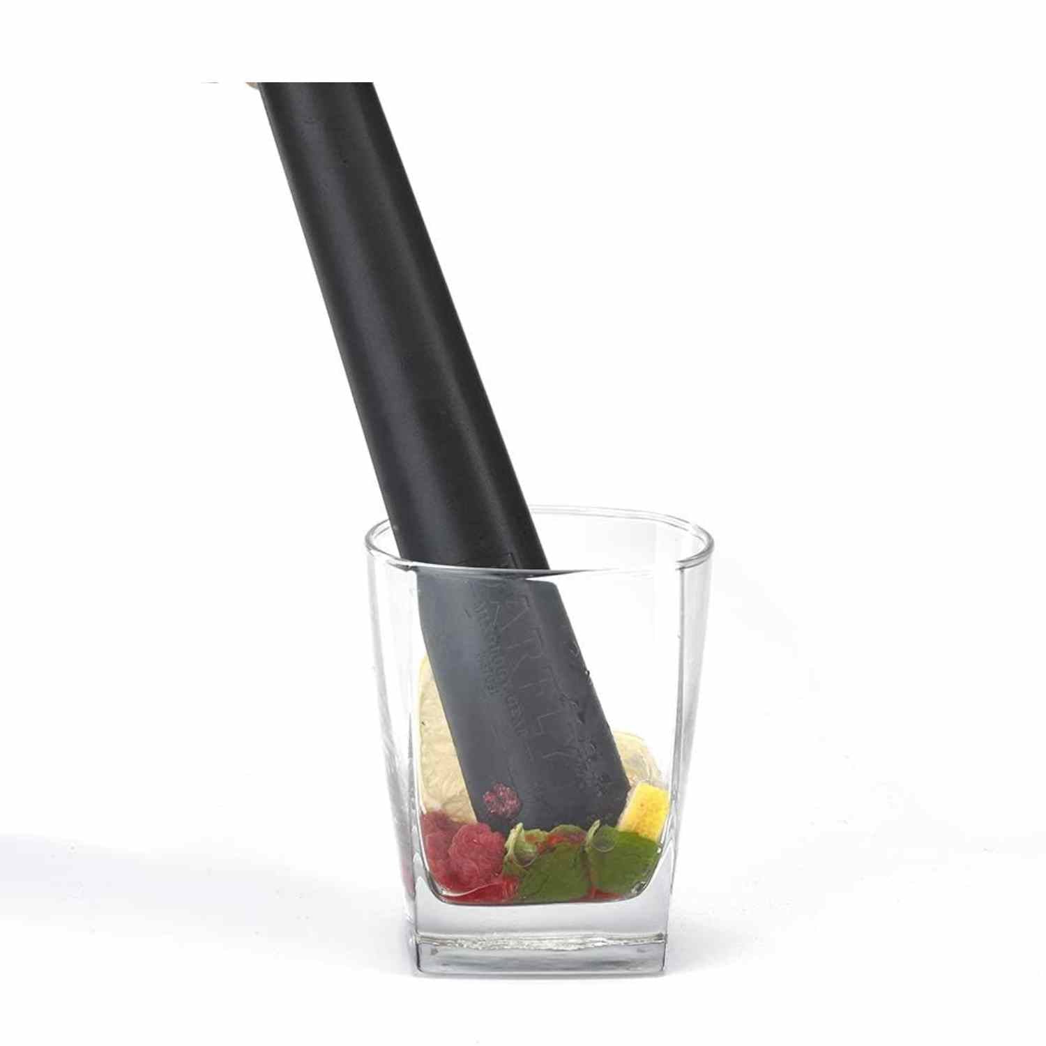 A 12-inch long, black composite bar muddler by Barfly, with a rounded base and a smooth handle, being used to crush berries, mint, and citrus slices at the bottom of a clear rocks glass