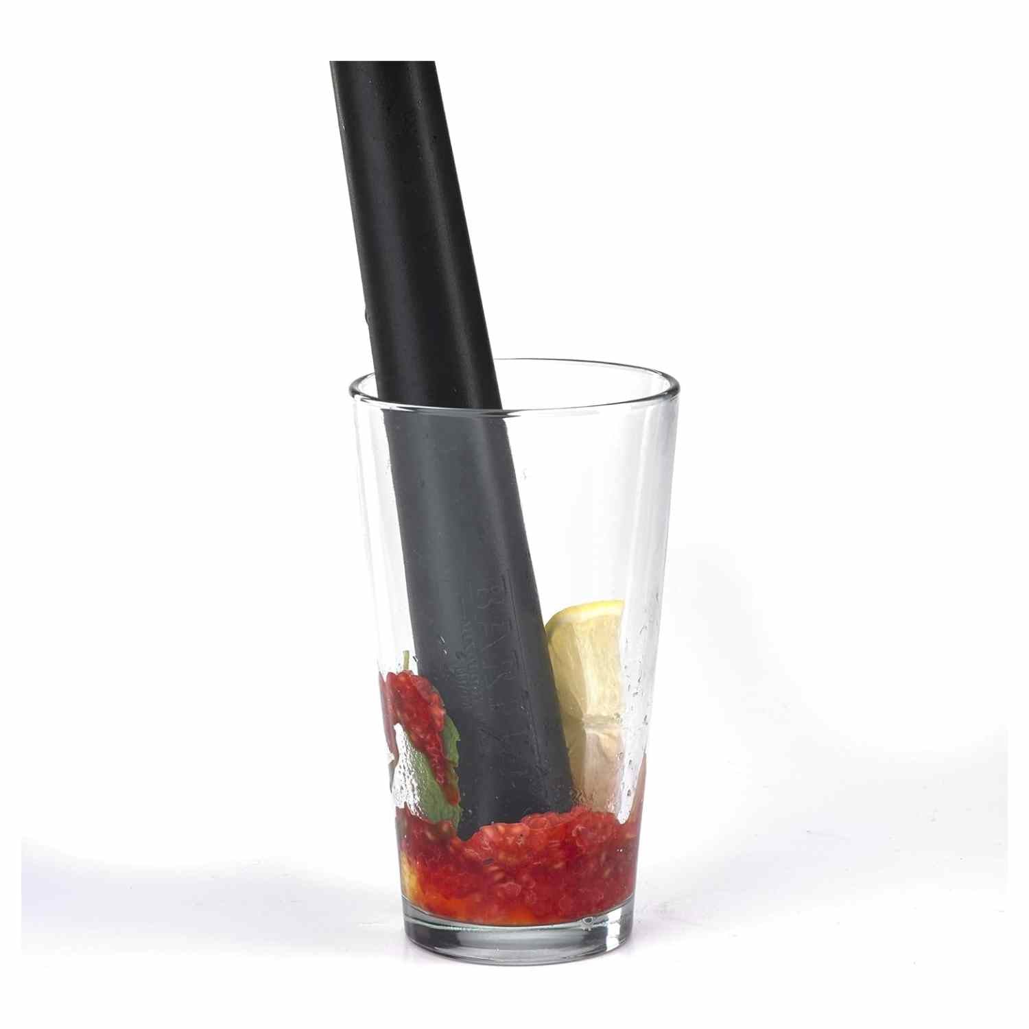 A 12-inch long, black composite bar muddler by Barfly, with a rounded base and a smooth handle crushing strawberries, raspberries, and mint in a tall, straight-sided clear glass.