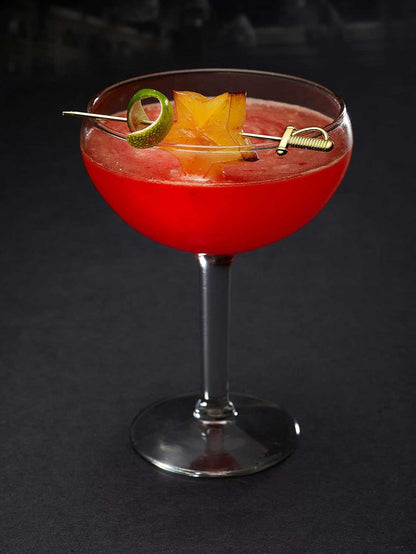 A bright red cocktail in a stemmed coupe glass, garnished with a lime twist and a starfruit slice, both skewered on a  4.5 inch Gold Plated Barfly Cocktail Pick, with a Sword top