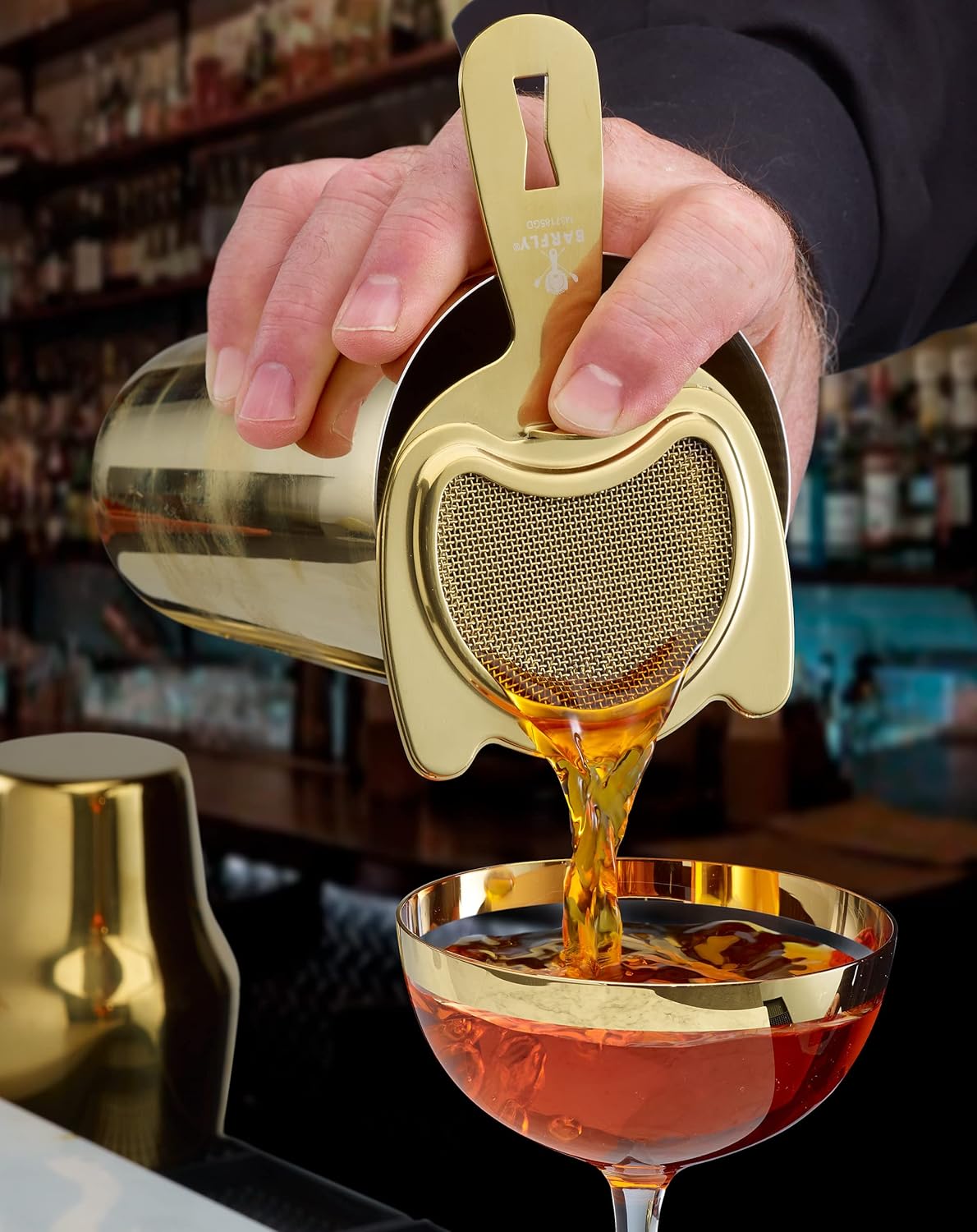 A bartender pouring a cocktail from a shaker with a Gold Plated Barfly Fine Mesh Spring Strainer on a glass with ice