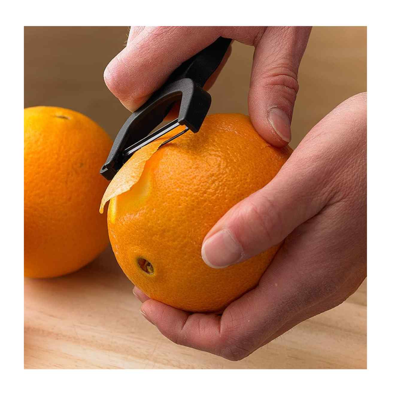 Person using a Black Mercer Culinary Y Swiss Peeler to remove skin from an orange on a wooden surface.